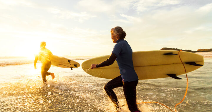 A couple runs along the water’s edge with their surfboards